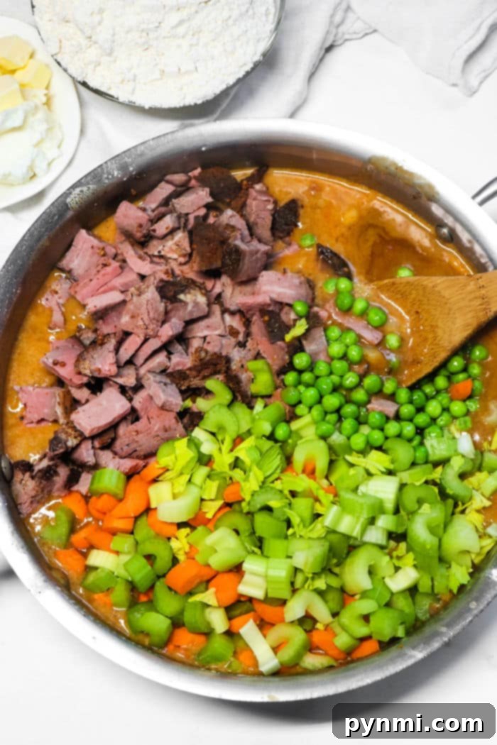 A pot filled with rich beef ingredients: chopped beef, vibrant peas, crisp carrots, tender celery, and a thick, savory sauce, perfectly reminiscent of a classic double crust beef pot pie filling.