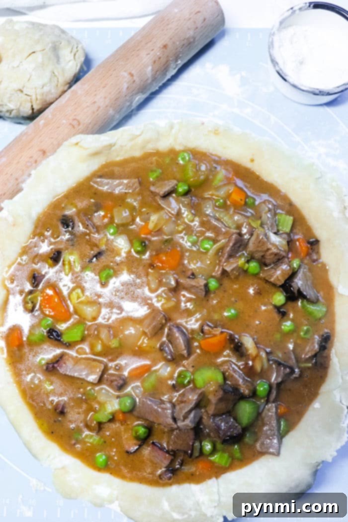 A partially filled double crust pot pie with a savory mixture of beef, peas, carrots, celery, and sauce. A wooden rolling pin and a small bowl of flour are ready nearby, with the top crust dough positioned at the top left corner, poised for assembly.