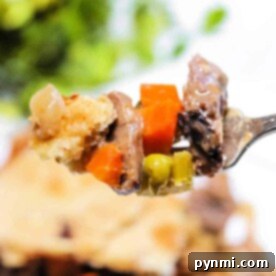 A fork holds a bite of double crust pot pie, showcasing peas, carrots, and crisp golden crust; blurred pie and vibrant greens create a cozy background.