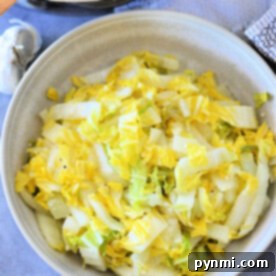 Napa Cabbage: Fresh Ideas and Recipes 6 A bowl of cooked napa cabbage sits on the table, accompanied by a pan and a hint of garlic in the background, offering a delightful glimpse into a simple yet flavorful recipe.