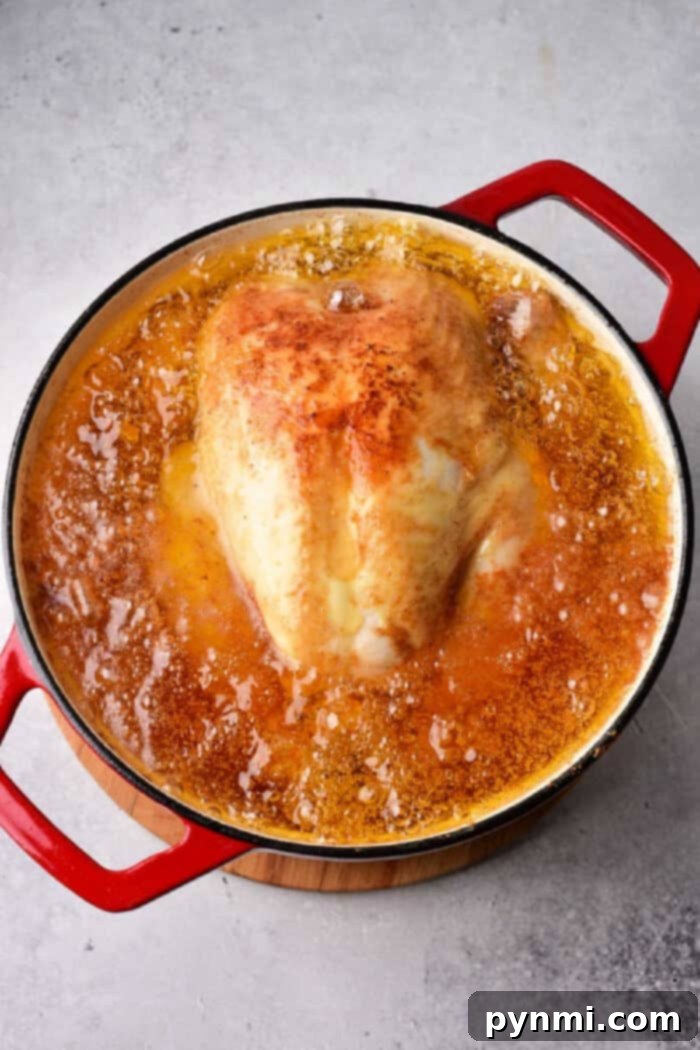 Crispy Whole Fried Chicken Feast 4 A whole fried chicken simmers in a pot of bubbling oil, viewed from above.