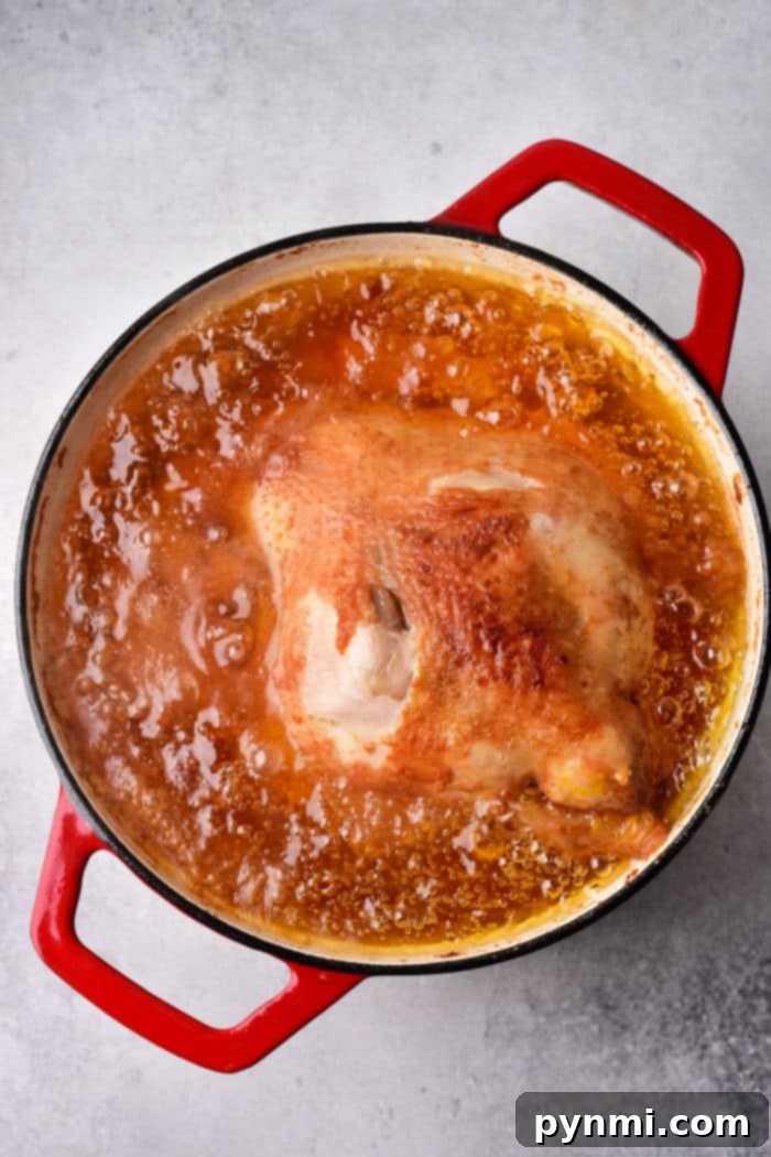 Crispy Whole Fried Chicken Feast 5 A whole fried chicken simmers in a red pot, enveloped in a rich golden-brown oil.