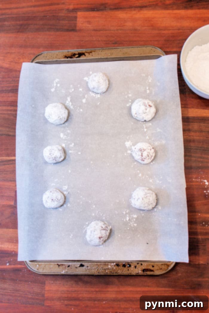 Red Velvet Crinkle Cookies from Cake Mix 4 Red Velvet Crinkle Cookies made from cake mix, these raw cookie dough balls are covered in powdered sugar and rest on a parchment-lined baking sheet.