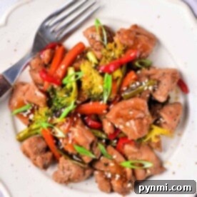 Savor the delicious Chicken Thigh Stir Fry featuring tender chicken, broccoli, bell peppers, and sesame seeds artfully arranged on a white plate with a fork.