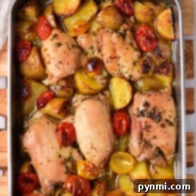 Mediterranean chicken thighs roasted with potatoes and cherry tomatoes in a metal pan on a wooden board.