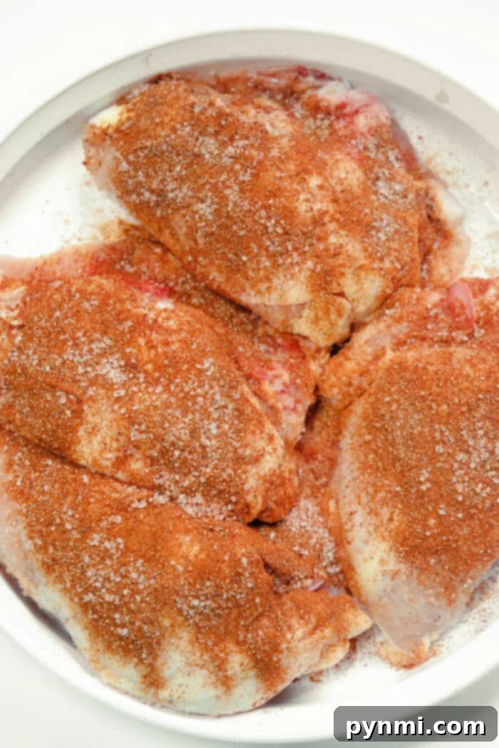 Raw chicken breasts generously coated with a reddish dry rub, ready for smoking on a Traeger grill.
