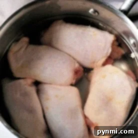 Raw chicken thighs sit in a stainless steel pot, preparing for the next step—wondering how long to boil chicken thighs for the perfect tenderness.
