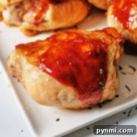 BBQ chicken thighs with a glossy glaze, garnished with herbs, served on a white square plate. Oven-baked to perfection.