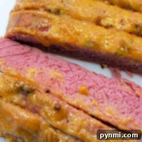 Sliced corned beef with a mustard topping rests on a white cutting board, offering a delightful twist on how to cook corned beef in the oven.