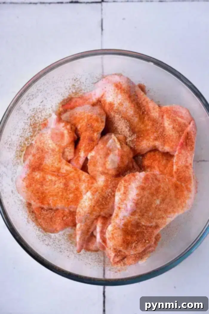 Golden Crispy Whole Chicken Wings 4 A glass bowl containing raw chicken wings, seasoned with a reddish spice mix, ready to be transformed into delicious baked whole chicken wings, sits on a white tiled surface.