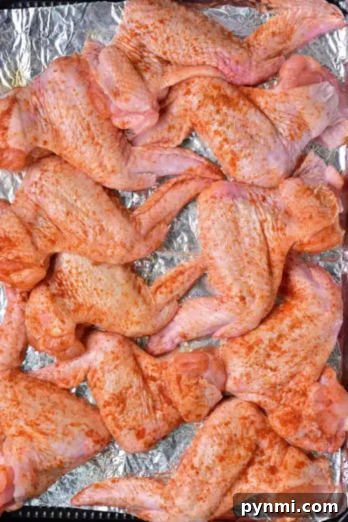Golden Crispy Whole Chicken Wings 5 Raw, seasoned whole chicken wings arranged on a foil-lined baking sheet, ready to be baked. The wings are covered with a red spice rub.