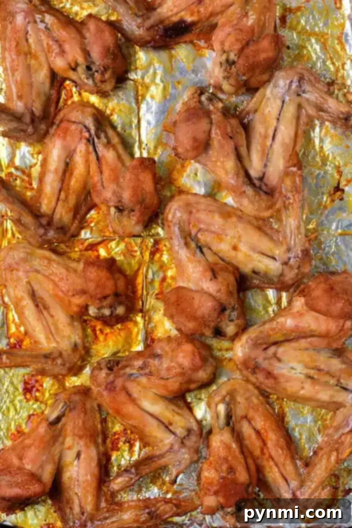 Golden Crispy Whole Chicken Wings 7 A baking sheet is covered with a layer of baked whole chicken wings. The wings are arranged in rows on a foil-lined tray and appear to be seasoned and baked until golden brown.