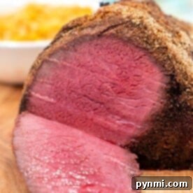 Close-up of a sliced Top Round Roast Recipe, featuring a crispy crust on a wooden board. Sides are blurred in the background.