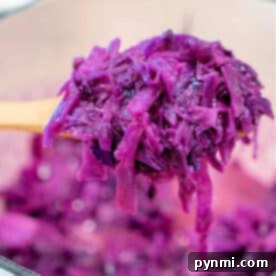 A wooden spoon holding sauteed red cabbage over a pot filled with more shredded cabbage, highlighting the rich purple color and tender texture.