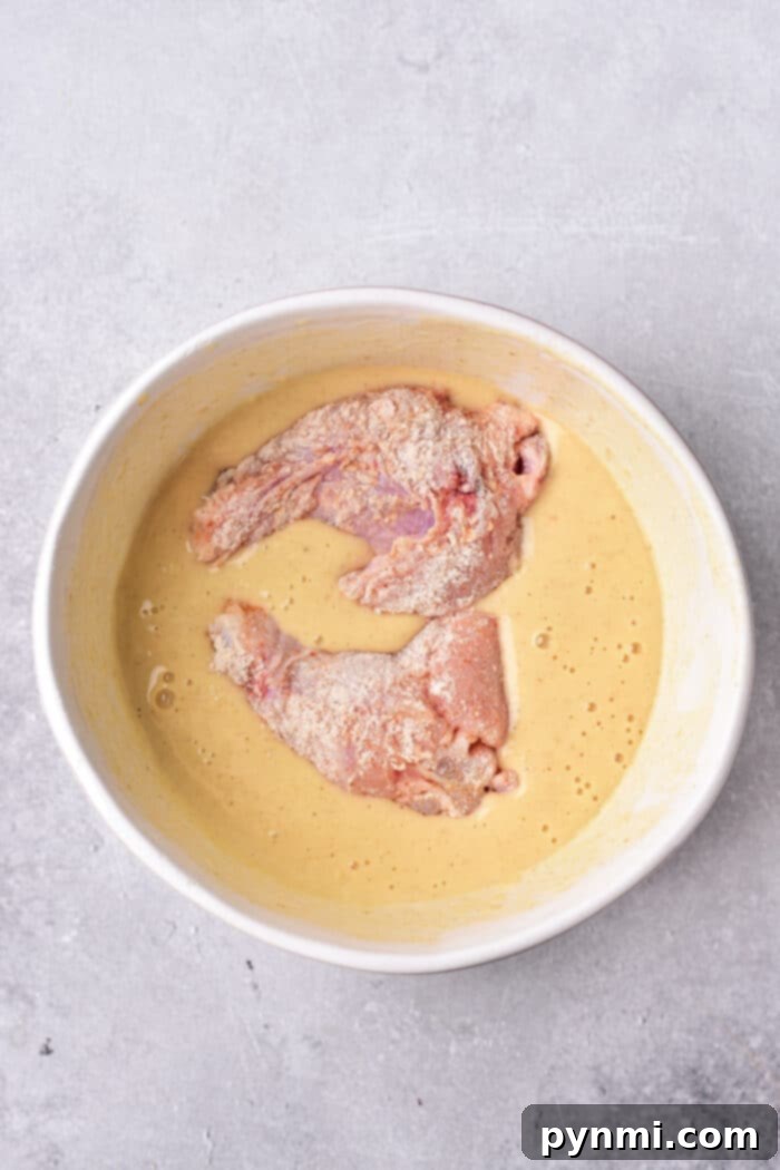 Raw chicken pieces in a creamy tempura batter sit invitingly in a round white bowl on a gray surface, while you ponder how long to deep fry chicken wings for that perfect crispiness.