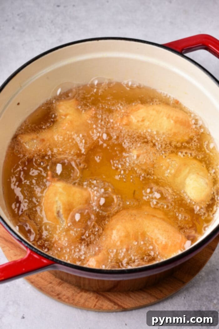 tempura chicken wings cook in hot oil inside a red pot placed on a wooden surface, much like the ambiance created when timing how long to deep fry chicken wings for that perfect crispy texture.