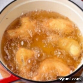tempura chicken wings cook in hot oil inside a red pot placed on a wooden surface, much like the ambiance created when timing how long to deep fry chicken wings for that perfect crispy texture.