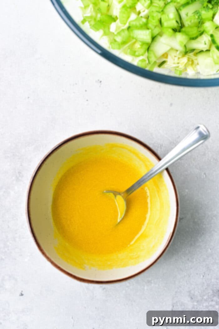 Effortless Asian Cabbage Slaw 4 A small bowl containing a vibrant yellow Dijon mustard dressing, ready to be poured over a fresh cabbage salad.