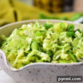 A speckled bowl is brimming with a refreshing cabbage salad, featuring chopped green cabbage and crisp slices of cucumber.