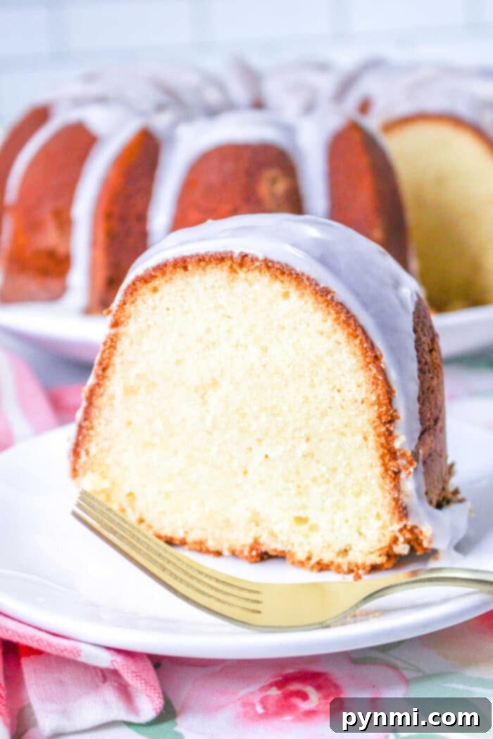 Homemade Sara Lee-Style Pound Cake 2 A slice of million dollar Pound Cake glazed bundt cake sits on a white plate with a gold fork, with the rest of the delicious cake in the background.