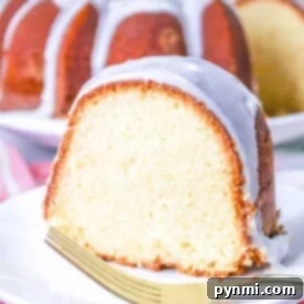 Slice of glazed bundt cake, reminiscent of a old fashioned million dollar Pound Cake, rests on a white plate with a gold fork, pink floral cloth underneath.