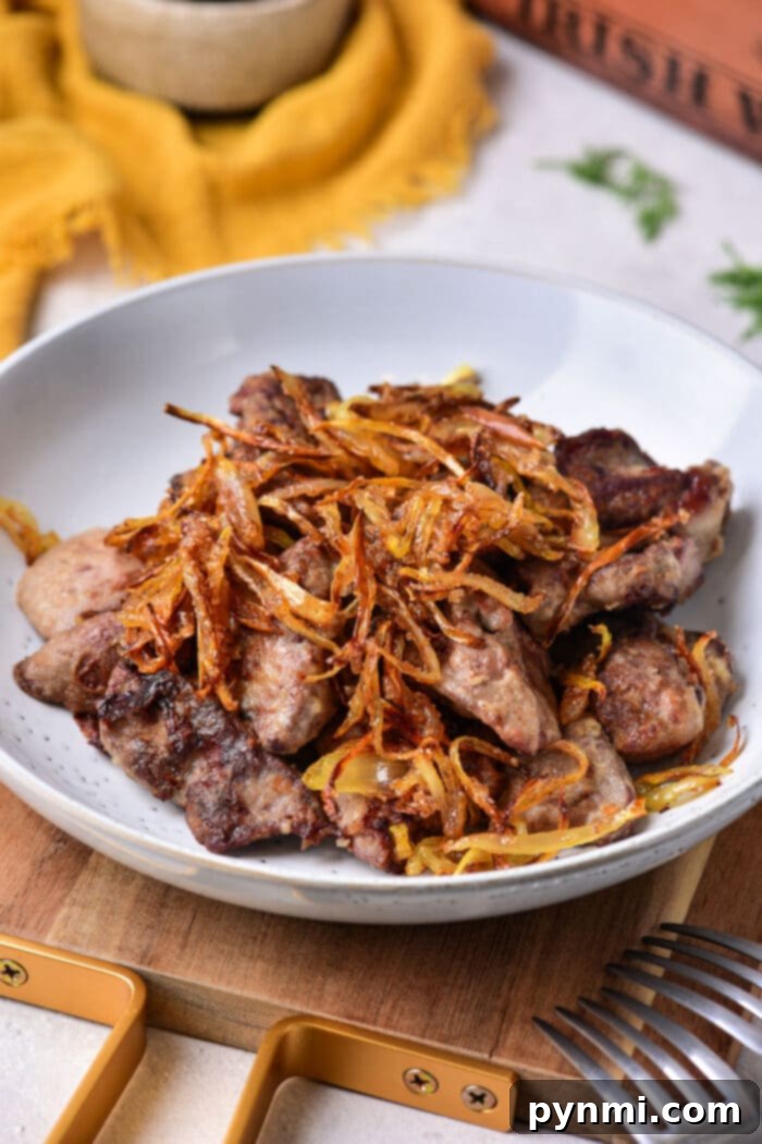 Mastering the Art of Chicken Liver 2 A plate of grilled chicken liver topped with crispy fried onions sits on the table, tempting you to pick up the nearby fork. This dish perfectly complements a guide on how to cook chicken liver to perfection.