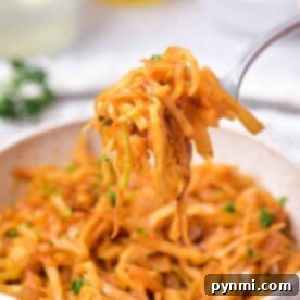 A fork holds a portion of sautéed shredded cabbage, perfectly embodying an Indian cabbage recipe, above a white bowl filled with more savory goodness. The dish is garnished with chopped herbs. In the blurred background, white bowls and clear bottles subtly enhance the scene.