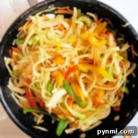 A skillet filled with sautéed mixed vegetables, featuring bell peppers, onions, and zucchini, takes inspiration from a Jamaican Cabbage Recipe.