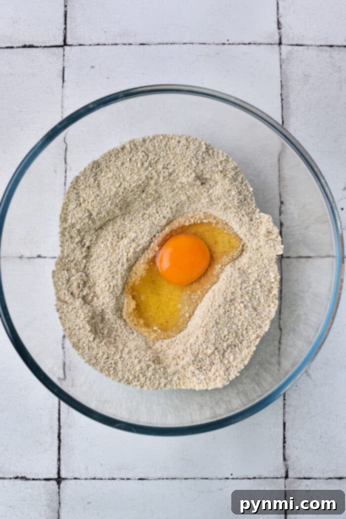 The Matzo Ball Demystified: History, How-To, and a Classic Recipe 4 A glass bowl with matzo meal and an egg in the center sits on a tiled surface, emblematic of the initial steps for matzo ball preparation.