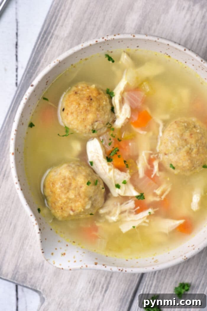A steaming bowl of traditional Chicken Matzo Ball Soup, garnished with fresh dill, sits on a rustic wooden table, inviting comfort and warmth.