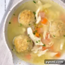 A bowl of rich Chicken Matzo Ball Soup sits invitingly on a wooden surface, brimming with tender chicken and vibrant vegetables.