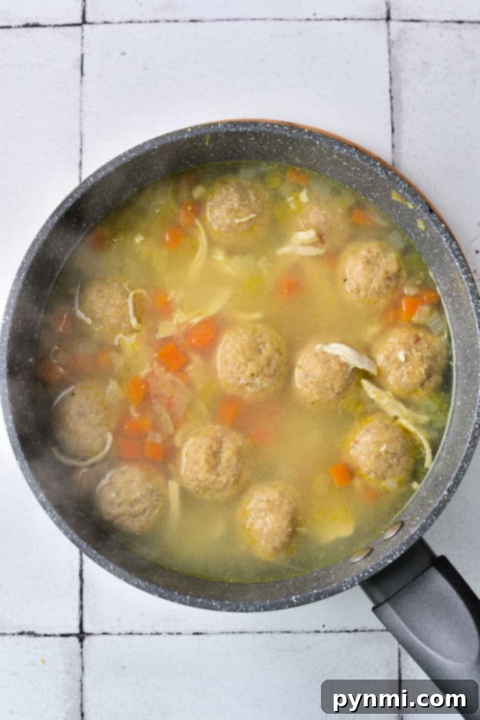 A close-up of a rustic bowl filled with golden Matzo Ball Soup, featuring tender chicken, fresh carrots, and a sprinkle of herbs.