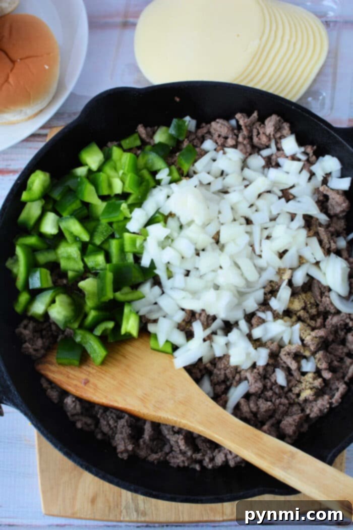 Philly Cheesesteak Sloppy Joes 4 Ground beef Philly Cheesesteak filling simmering in a cast iron skillet, topped with melting provolone cheese.