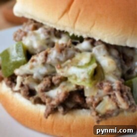 Close-up of a Sloppy Joe sandwich with ground beef, melted cheese, and green peppers on a white plate, evoking the savory essence of a Philly Cheesesteak.