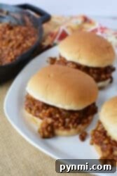 Three Sloppy Lentil Joes sit on a white plate beside a skillet, all resting on a woven mat.