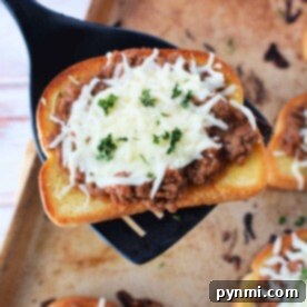 A slice of Texas toast topped with savory meat sauce and melted cheese, garnished with parsley, sits enticingly on a spatula over a baking sheet.