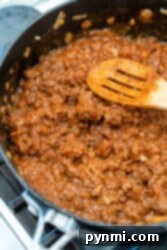 Cooking ground beef with onions and tomato sauce in a pan, stirred gently with a wooden spoon.