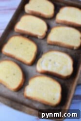A baking sheet with eight slices of Texas toast, each coated in butter, set on a light wooden surface.
