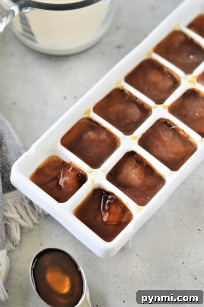A hand reaching for a clear glass of perfectly blended frozen coffee, highlighting its appealing texture.