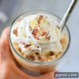 Close-up of a hand holding a frozen iced coffee topped with whipped cream and chocolate shavings, with a spoon.