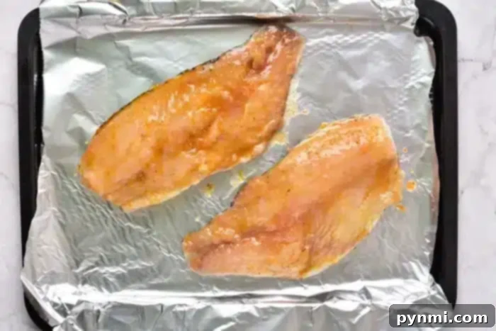 Two raw fish fillets, perfectly sauced, are placed on a foil-lined baking tray, ready to transform into a delightful meal as they bake from frozen.