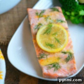 Complete Salmon Dinners: Recipes and Perfect Pairings 5 Salmon fillet garnished with a lemon slice and dill on a white plate, showcasing one of our delightful salmon dinner recipes, accompanied by broccoli in the background.