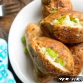 Baked potatoes with chopped green onions on a white plate, next to a fork and a blue patterned napkin, are perfect for those who wonder how long to cook a baked potato in the microwave. Enjoy this simple yet satisfying meal in just minutes.