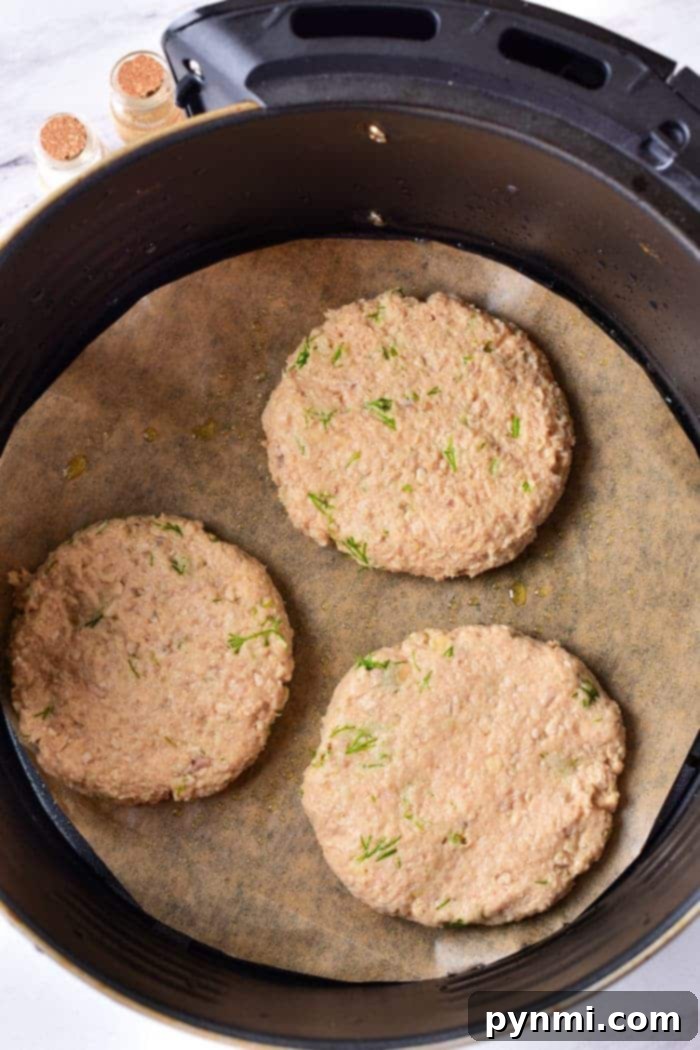 Mastering Ground Turkey 3 Three raw turkey burger patties in an air fryer with a parchment paper lining, ready to transform into a delicious meal. Curious about how long to cook ground turkey? It's simple—just adjust the time for juicy goodness and enjoy perfectly cooked patties every time.