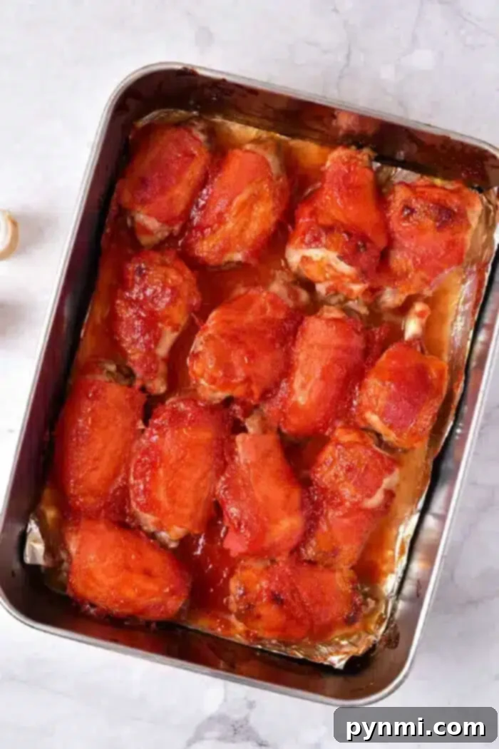 Chicken wings covered in a red sauce, possibly marinara or barbecue sauce, sits on a light-colored countertop to bake in oven.