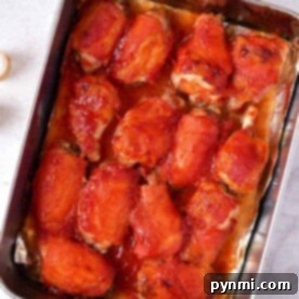 Baked chicken wings topped with barbecue sauce rest in a rectangular metal tray on a marble surface, perfectly cooked like you’d time wings in the oven.