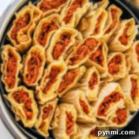 A pot filled with neatly arranged, uncooked red tamales wrapped in corn husks.