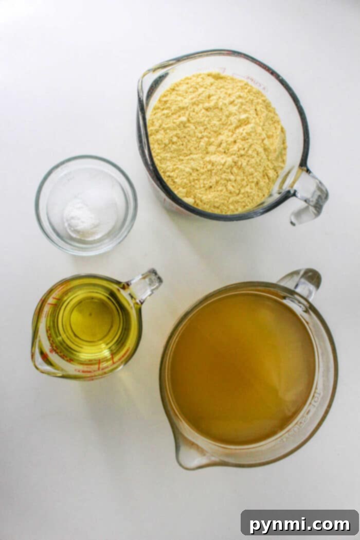Crafting Perfect Tamales Masa 3 Four measuring cups filled with cornmeal, oil, broth, and salt are arranged on a white surface, showcasing the essential ingredients for how to make tamales masa.