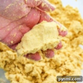 A hand expertly crumbles masa over a bowl filled with the same rustic dough, perfecting the art of making tamales.