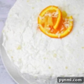 White frosted cake topped with vibrant orange slices and a sprinkle of shredded coconut, reminiscent of a luscious Hawaiian Pineapple Cake, presented elegantly on a white plate.